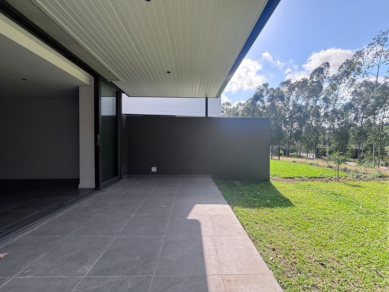 A modern covered patio featuring large format floor tiles, recessed lighting, and seamless access to the garden through wide sliding glass doors.