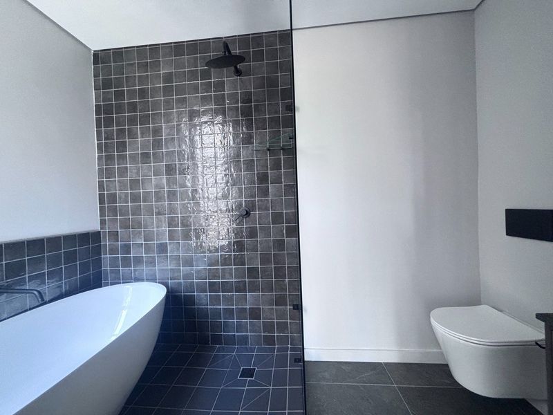 Modern bathroom featuring a sleek freestanding bathtub, a spacious walk-in shower with dark tiled accents, and a wall-mounted toilet.