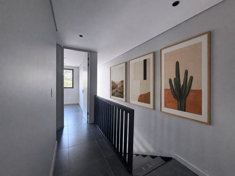A modern, well-lit hallway featuring sleek tiled flooring, a black metal balustrade overlooking the staircase, and clean, minimalist wall finishes.