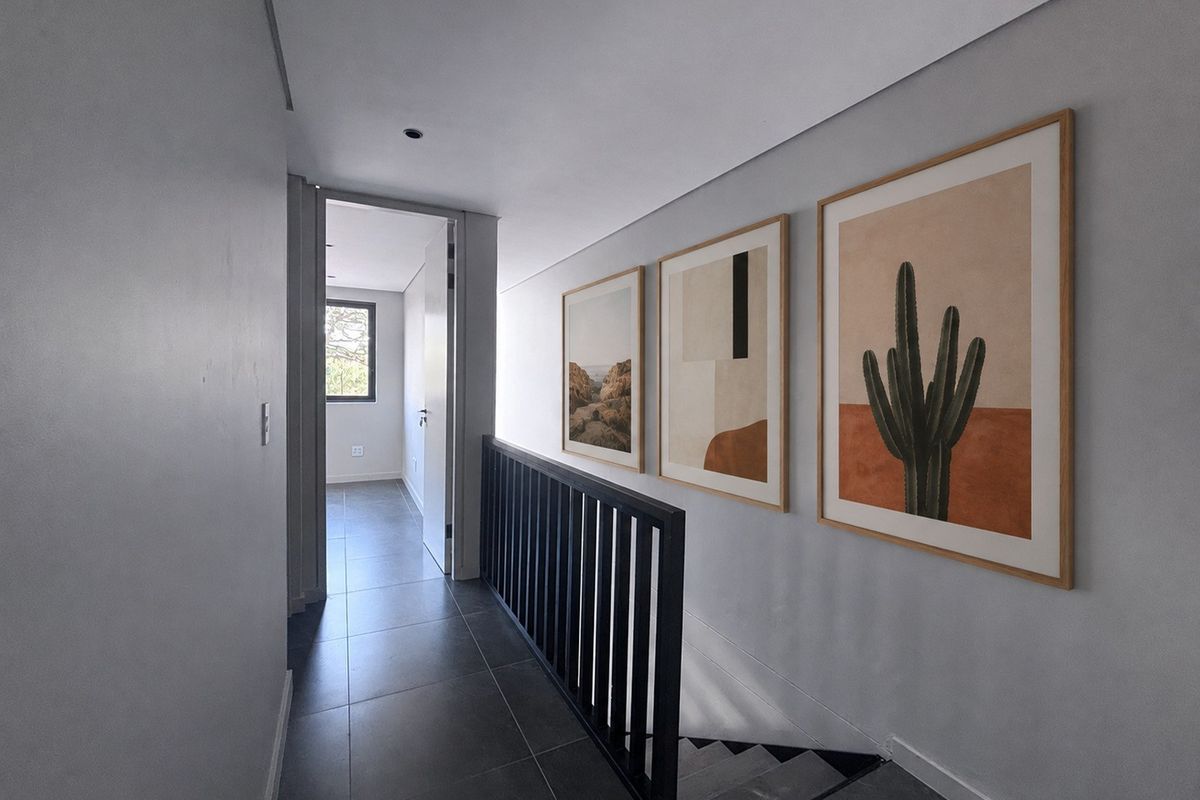 A modern, well-lit hallway featuring sleek tiled flooring, a black metal balustrade overlooking the staircase, and clean, minimalist wall finishes.