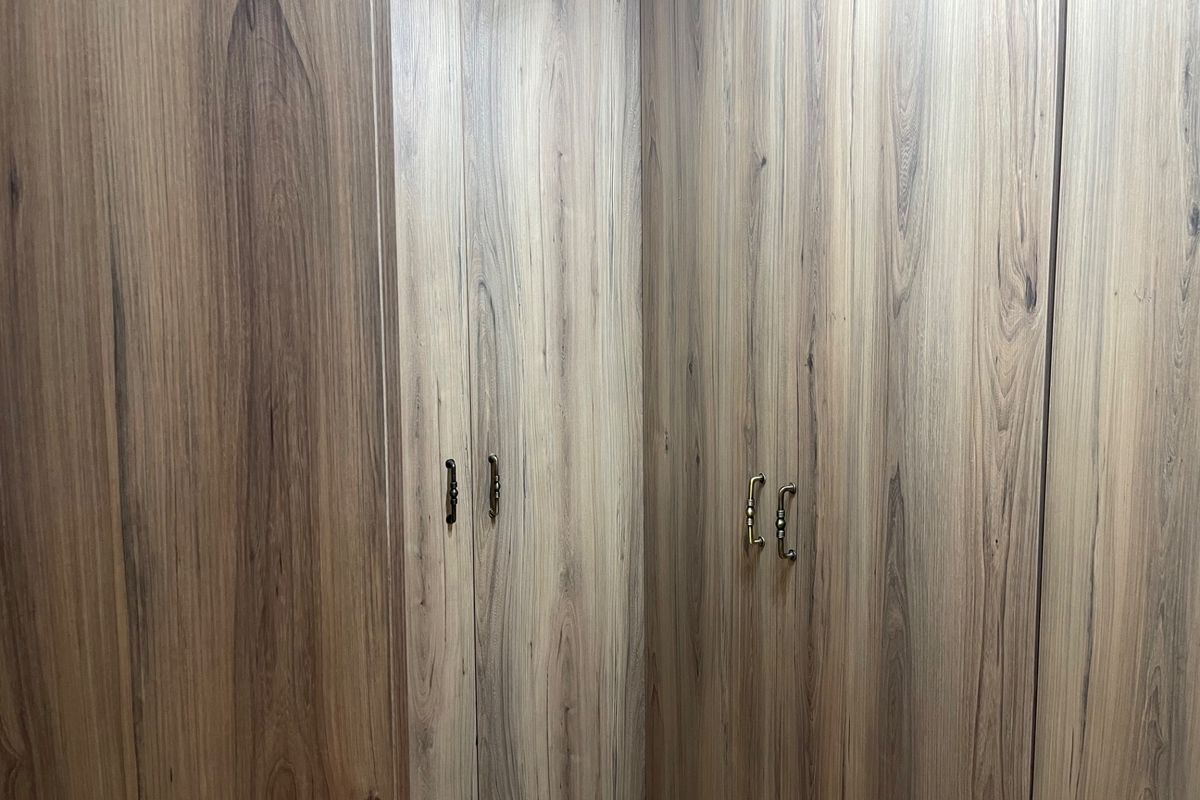 A close-up view of modern, wood-grain built-in cupboards with classic metal handles, providing ample storage space within the bedroom.