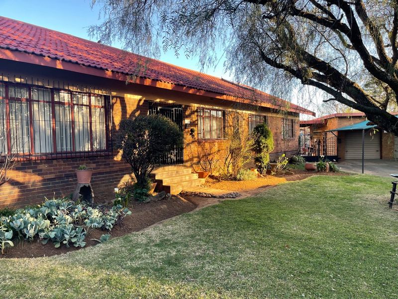 Front view of a brick house featuring a tiled roof, security bars on windows, and a well-maintained garden with an adjacent carport.