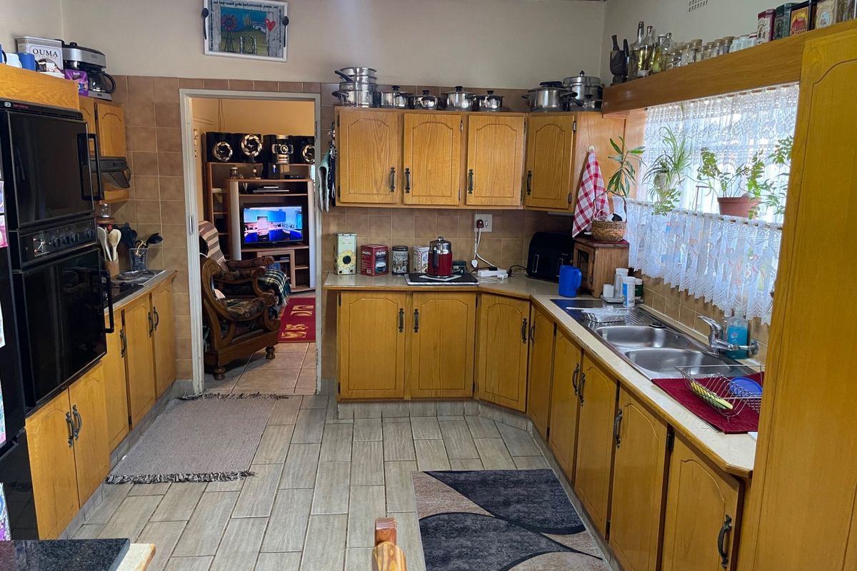 A functional kitchen featuring traditional wooden cabinetry, a double bowl sink, built-in eye-level oven, and tiled finishes throughout.