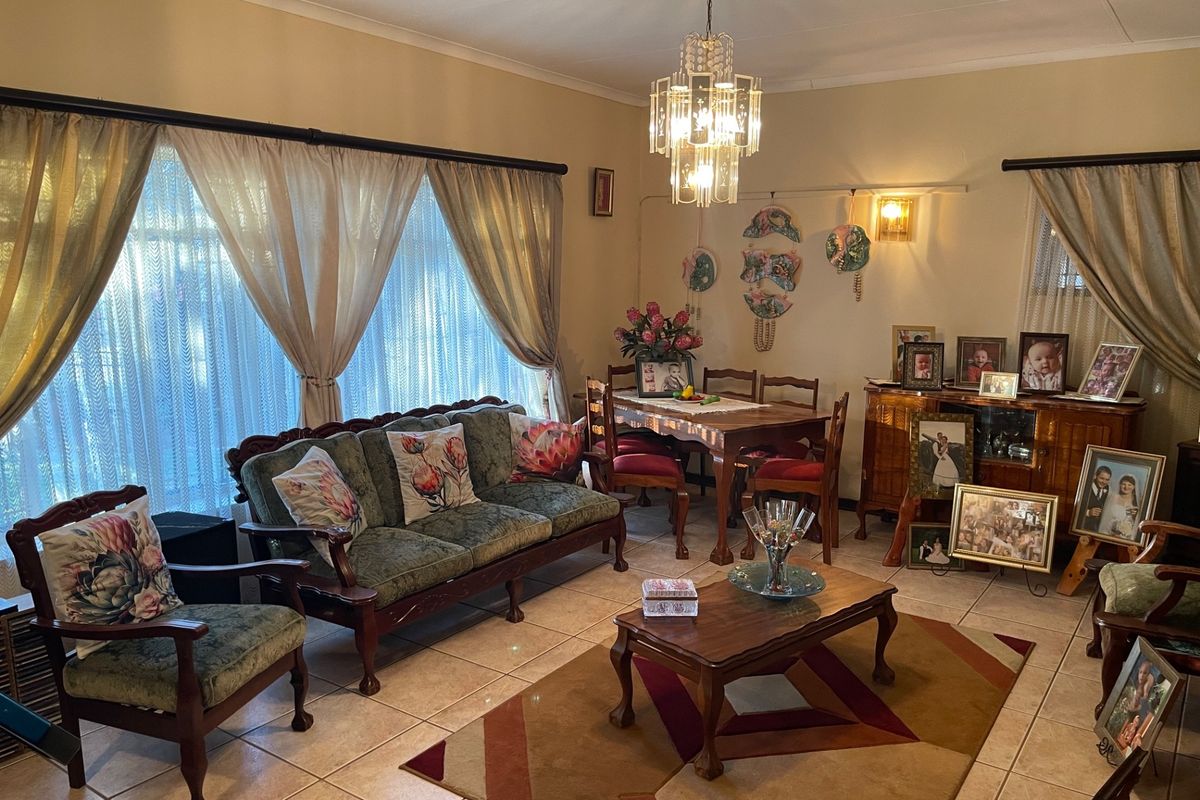 A spacious living and dining area featuring ceramic tile flooring, a decorative crystal chandelier, and large windows with curtain treatments.