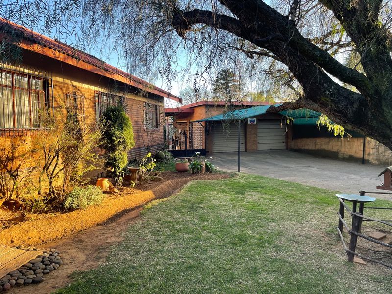 Rear view of the property featuring a brick exterior, established garden, lawn area, and a double garage with an attached carport.