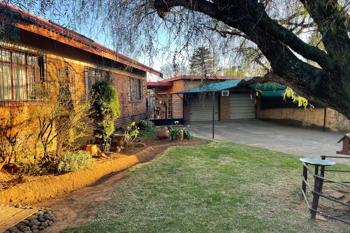 Rear view of the property featuring a brick exterior, established garden, lawn area, and a double garage with an attached carport.