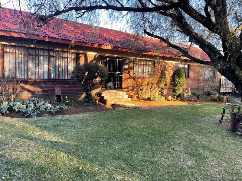 Front view of a single-story brick house featuring a tiled roof, security gates, and a well-maintained front garden area.