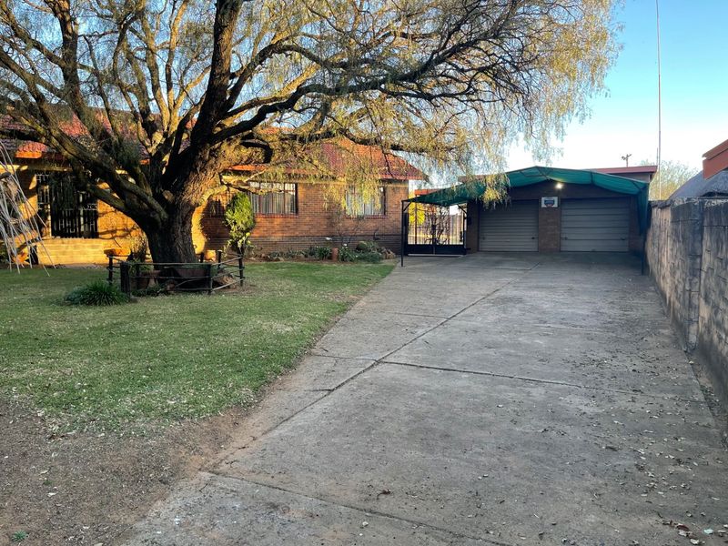 Front view of a brick house featuring a large mature tree, a concrete driveway, and a double garage with a covered carport area.