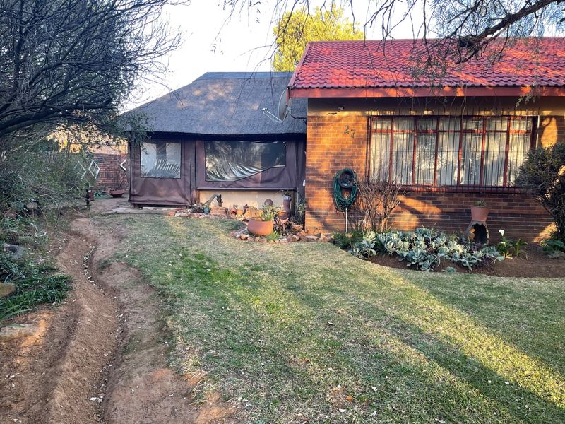 Rear view of the property featuring a combination of brick and thatched roofing, with a lawn area and an outdoor canvas-enclosed patio space.