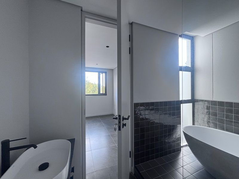 Modern bathroom featuring a freestanding bathtub, vessel sink with black matte fixtures, and dark tiled accents, leading into an adjacent bedroom space.