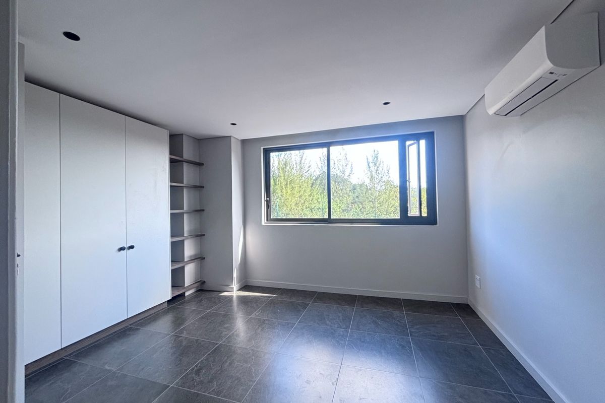 A bright, modern bedroom featuring tiled flooring, built-in cabinetry with open shelving, and a wall-mounted air conditioning unit.