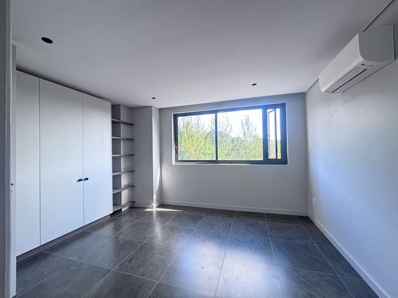 A bright, modern bedroom featuring tiled flooring, built-in cabinetry with open shelving, and a wall-mounted air conditioning unit.