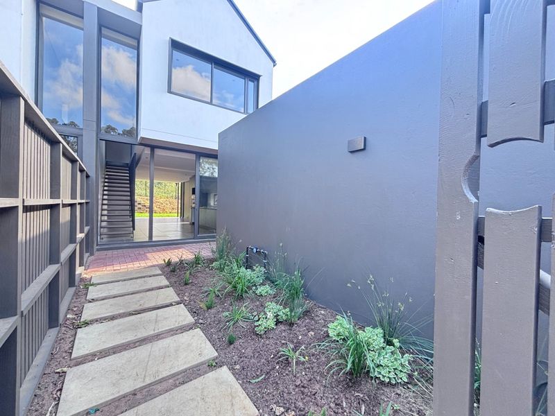A modern townhouse rear exterior featuring a paved walkway, landscaped garden bed, and large sliding glass doors leading into the interior living space.