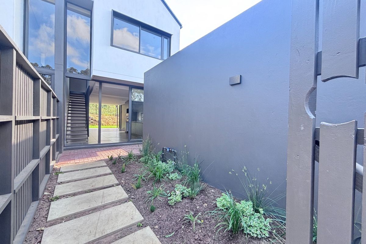 A modern townhouse rear exterior featuring a paved walkway, landscaped garden bed, and large sliding glass doors leading into the interior living space.