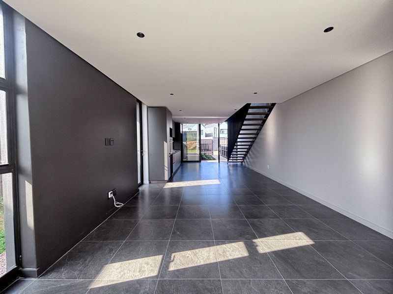 Spacious open-plan living and kitchen area featuring modern dark floor tiles, recessed lighting, and a sleek staircase leading to the upper level.