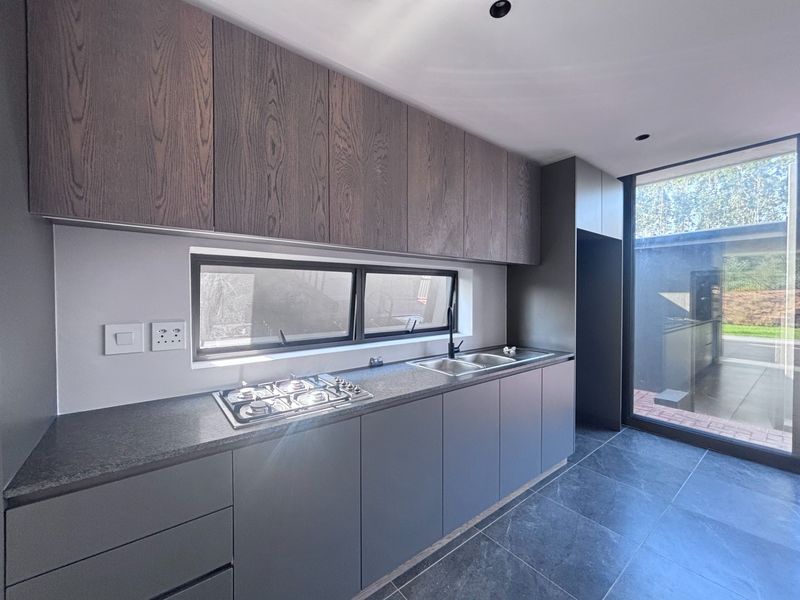 Modern kitchen featuring sleek dark cabinetry, stone countertops, a gas hob, and large windows providing natural light and garden views.