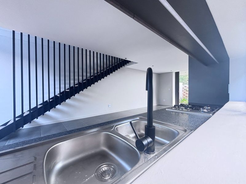 Modern kitchen area featuring a double bowl sink, gas hob, and a striking black metal staircase balustrade in an open-plan layout.