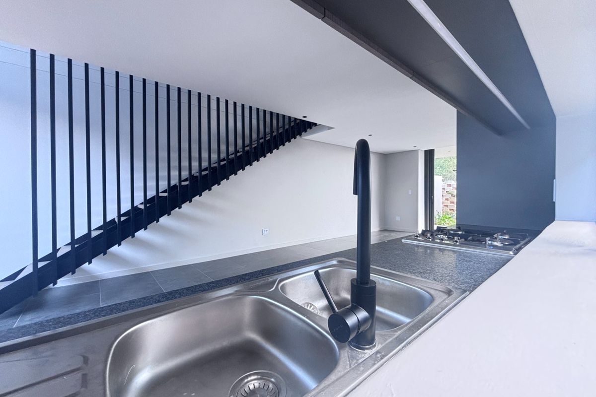 Modern kitchen area featuring a double bowl sink, gas hob, and a striking black metal staircase balustrade in an open-plan layout.