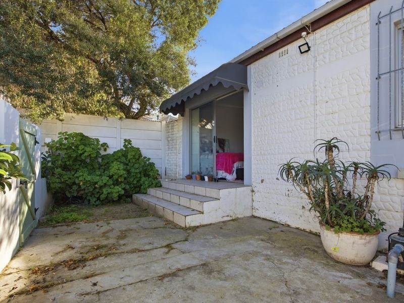 Rear exterior view featuring a concrete patio, tiled steps leading to a sliding glass door, and a private garden area with boundary walling.