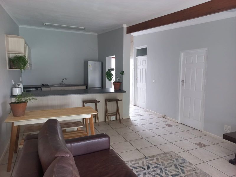 Open-plan living area featuring a kitchen with breakfast bar, tiled flooring, and exposed timber ceiling beam, leading to adjacent rooms.
