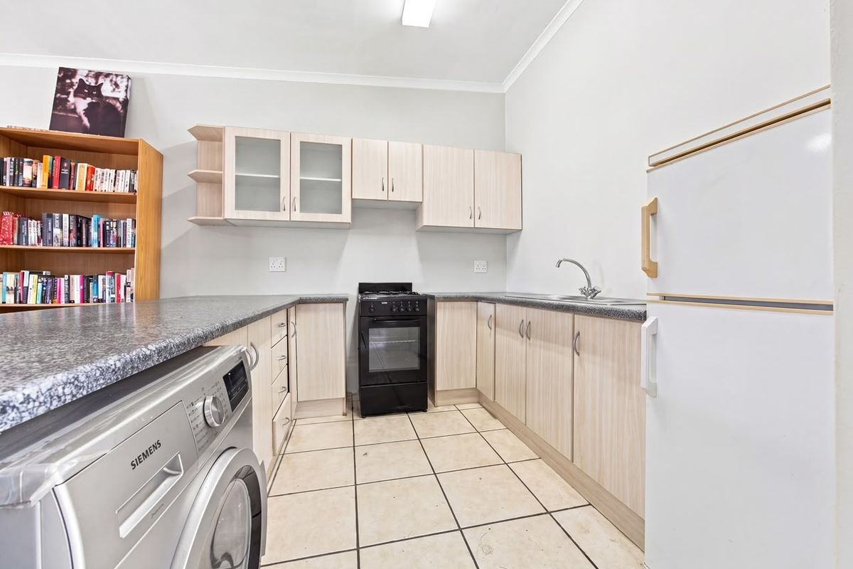 Functional kitchen featuring light wood-tone cabinetry, granite-look countertops, a stainless steel sink, and a freestanding oven, with tiled flooring throughout.