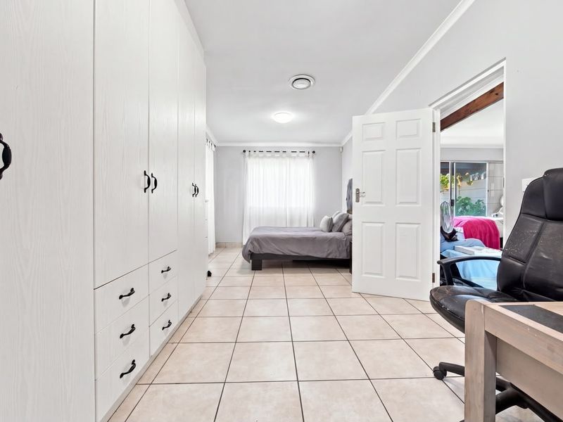 Spacious bedroom featuring extensive built-in cabinetry, neutral tiled flooring, and direct access to an adjoining room.