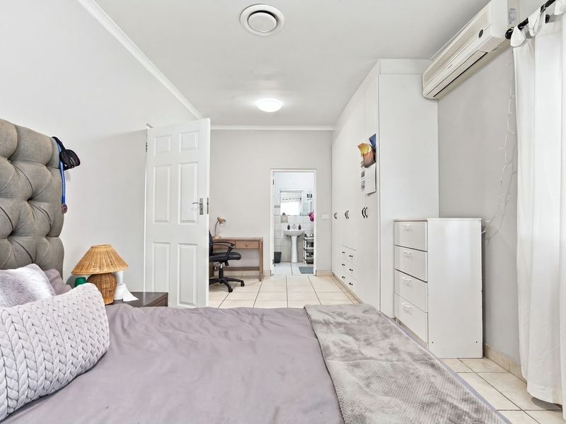 A well-maintained bedroom featuring built-in cupboards, tiled flooring, and a split-system air conditioner, with an adjoining en-suite bathroom visible.