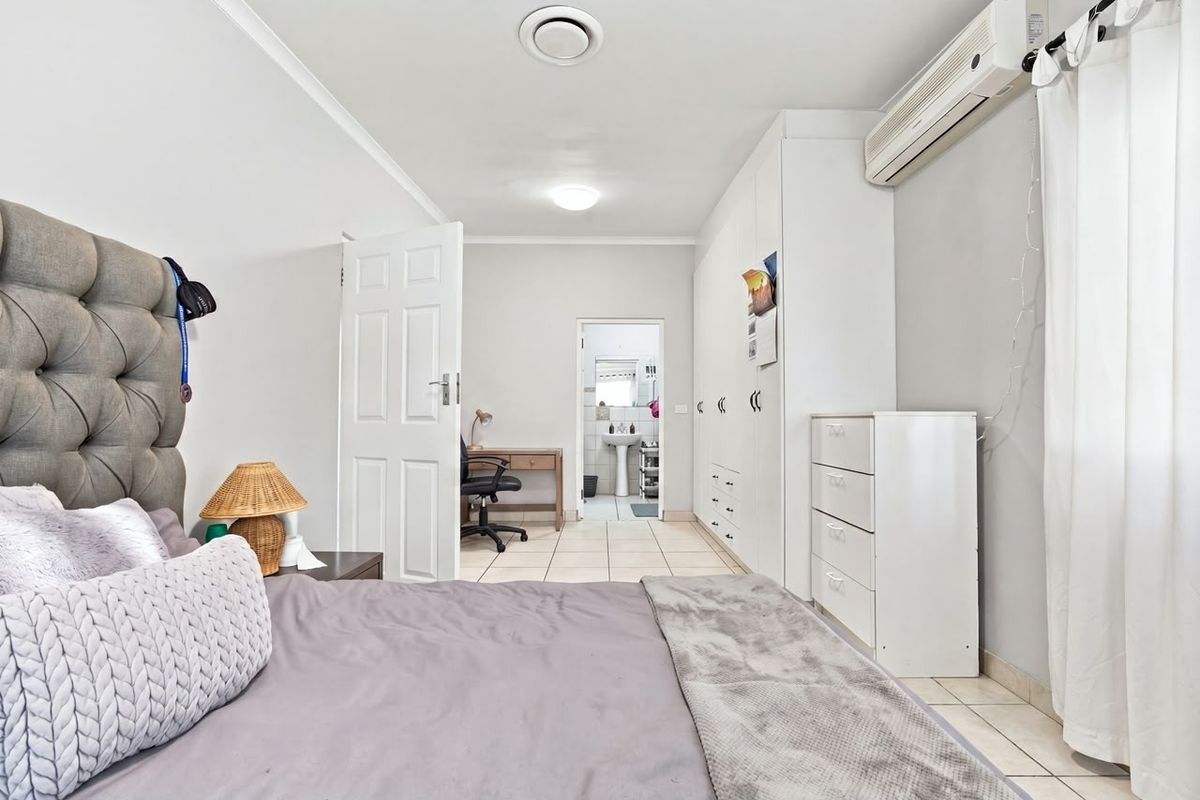 A well-maintained bedroom featuring built-in cupboards, tiled flooring, and a split-system air conditioner, with an adjoining en-suite bathroom visible.