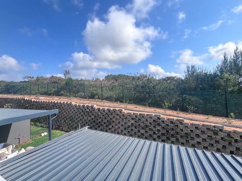 Rear view of the property featuring a tiered retaining wall, secure electric fencing, and a corrugated metal roof structure.