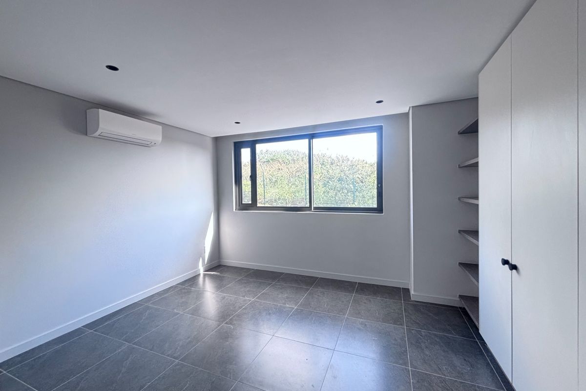 A bright, modern, and empty bedroom featuring neutral tiled flooring, built-in storage, and an integrated air conditioning unit.