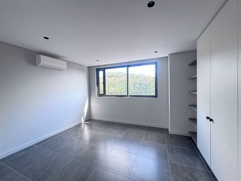 A bright, modern, and empty bedroom featuring neutral tiled flooring, built-in storage, and an integrated air conditioning unit.