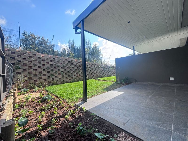 A modern covered patio featuring tiled flooring and recessed lighting, overlooking a private garden with a structured retaining wall.