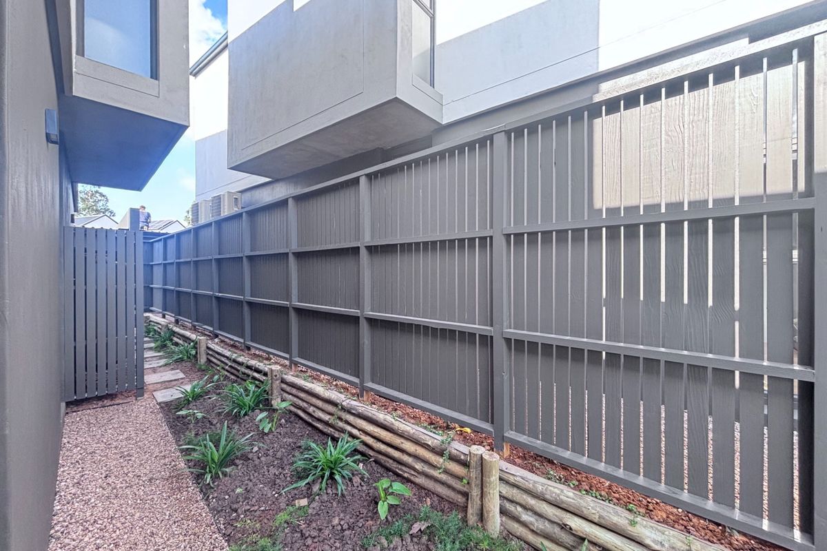 A side passage featuring a modern timber slat fence, a timber sleeper retaining wall, and a gravel pathway alongside the townhouse structure.