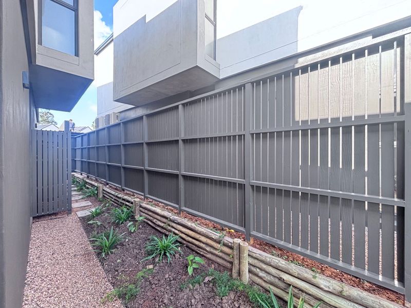A side passage featuring a modern timber slat fence, a timber sleeper retaining wall, and a gravel pathway alongside the townhouse structure.