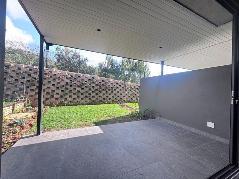 A modern covered patio featuring large format floor tiles, recessed lighting, and a view of the private garden and retaining wall.