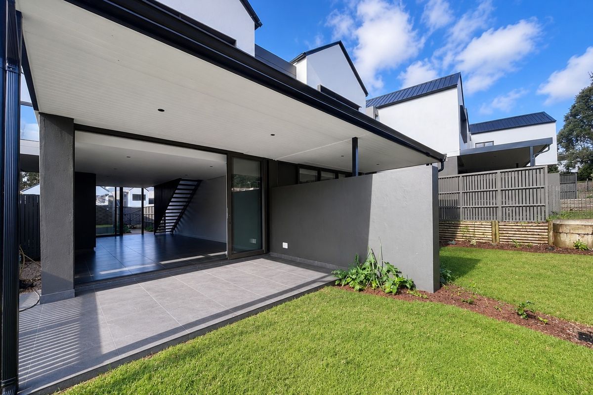 A modern rear exterior view of a townhouse featuring a covered tiled patio, seamless indoor-outdoor flow, and a well-maintained private garden.