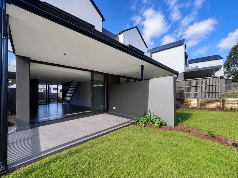 A modern rear exterior view of a townhouse featuring a covered tiled patio, seamless indoor-outdoor flow, and a well-maintained private garden.