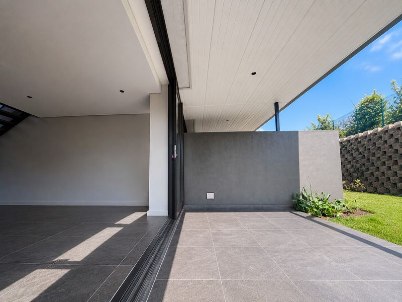 A modern, covered patio featuring large format floor tiles, recessed lighting, and seamless access to the garden through sliding glass doors.