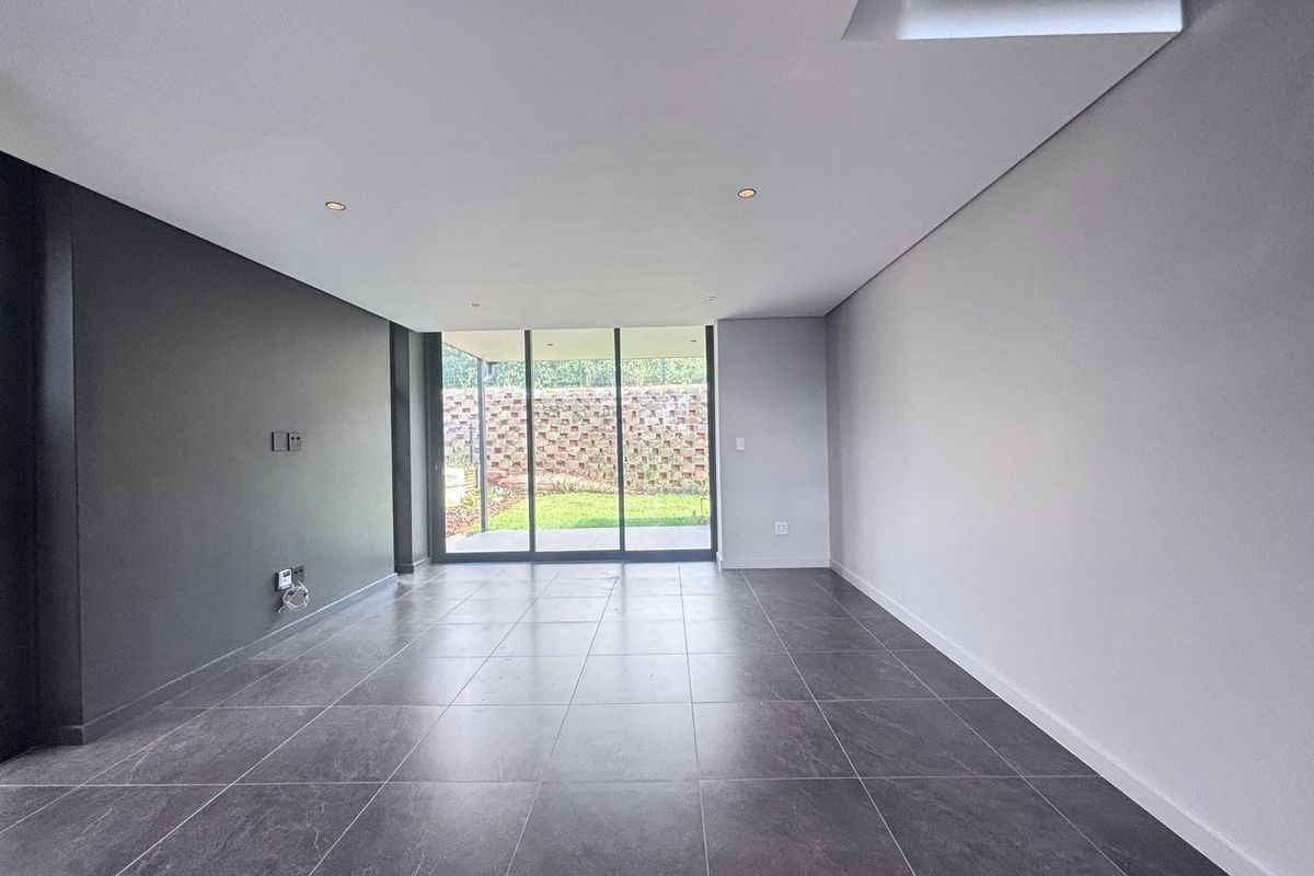 A modern, empty living room featuring large format floor tiles, recessed lighting, and sliding glass doors providing access to the rear garden.