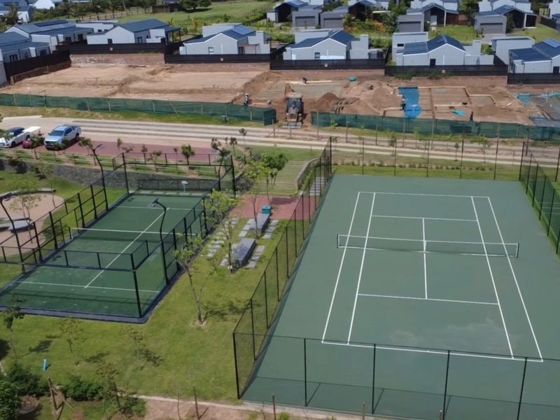 Aerial view of a residential estate sports facility featuring a well-maintained tennis court and a padel court with perimeter fencing.