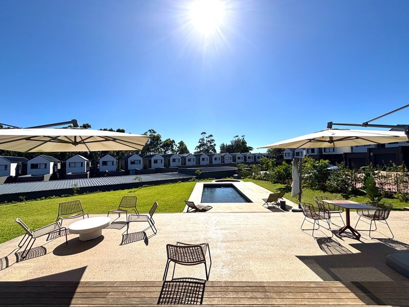 Spacious outdoor entertainment area featuring a paved patio, timber decking, a swimming pool, and a well-maintained lawn in a townhouse complex.