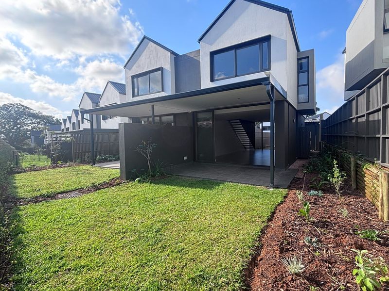 Modern townhouse rear elevation featuring a covered patio, sliding glass doors, and a well-maintained landscaped garden with timber fencing.