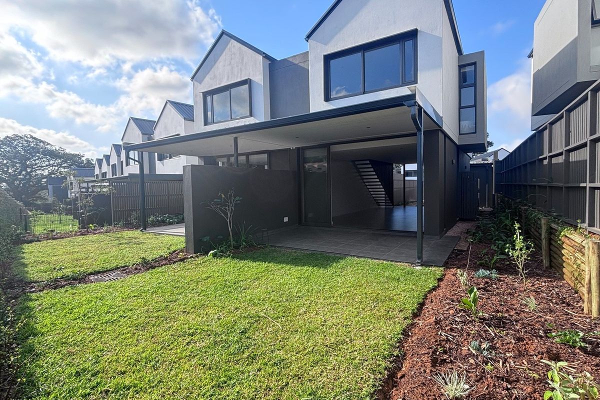 Modern townhouse rear elevation featuring a covered patio, sliding glass doors, and a well-maintained landscaped garden with timber fencing.