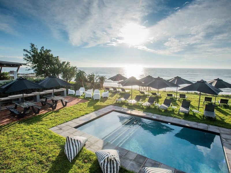 Outdoor pool area featuring a swimming pool with stone coping, brick paving, and expansive lawn overlooking the ocean.