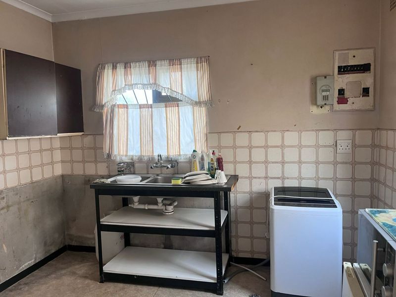 A functional laundry area featuring a double stainless steel sink, tiled splashback, and an exposed electrical distribution board, requiring cosmetic updates.