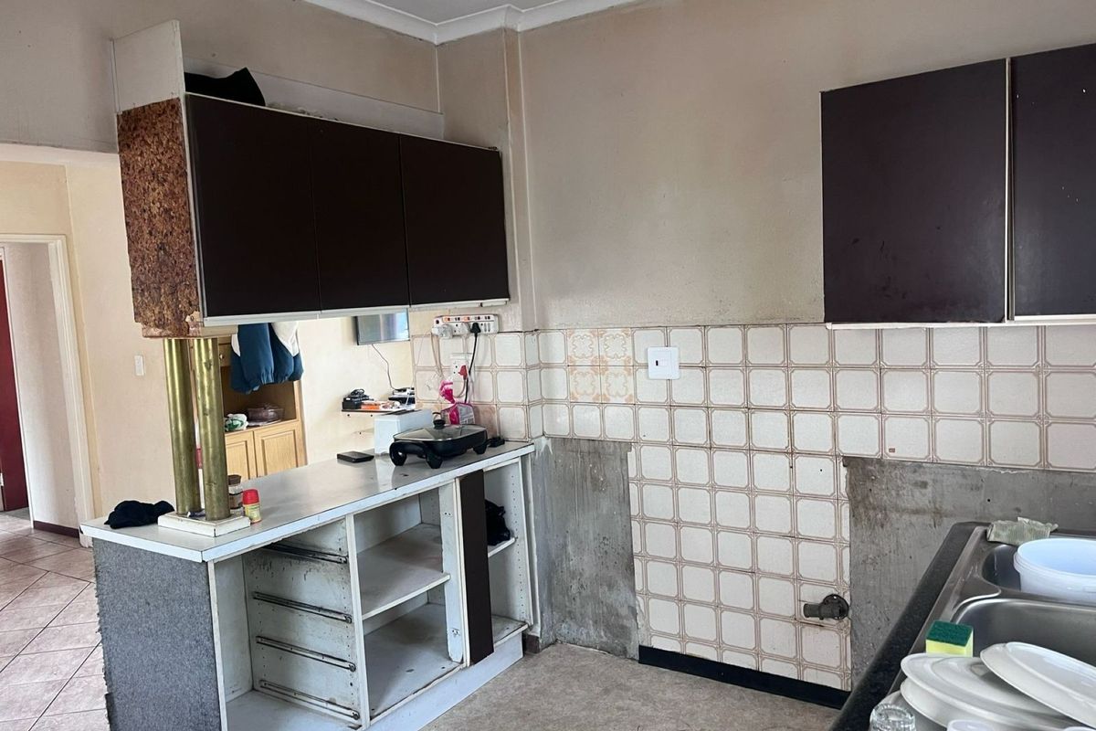 A dated kitchen area featuring original cabinetry, a tiled backsplash, and a double bowl sink, currently requiring significant renovation and cosmetic updates.
