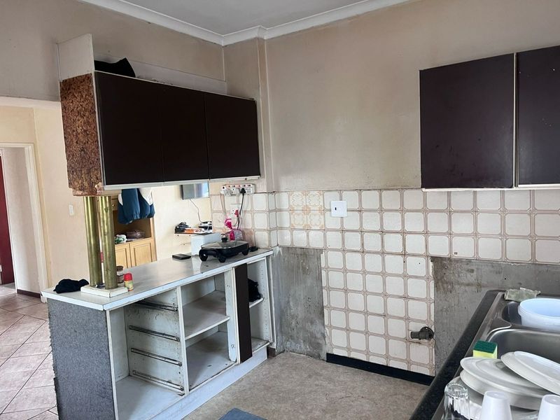 A dated kitchen area featuring original cabinetry, a tiled backsplash, and a double bowl sink, currently requiring significant renovation and cosmetic updates.