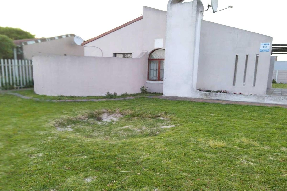 Rear view of the property featuring a lawn area, exterior wall with chimney, and an arched window.