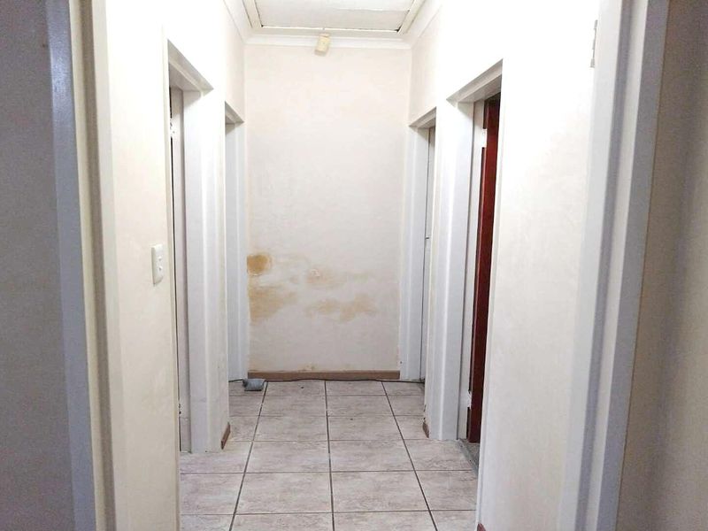 A vacant hallway featuring tiled flooring and multiple doorways, showing visible signs of water damage on the end wall.