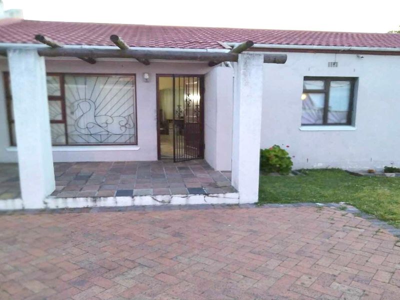 Front exterior view of a single-story house featuring a paved driveway, a covered patio with a timber pergola, and security features on windows and doors.